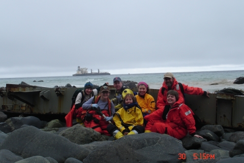 A group of people in response gear sitting on a rocky shoreline with a boat in the background on the horizon.