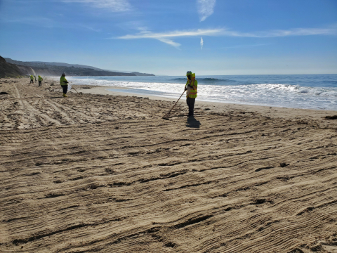 Cleanup workers raking a beach.