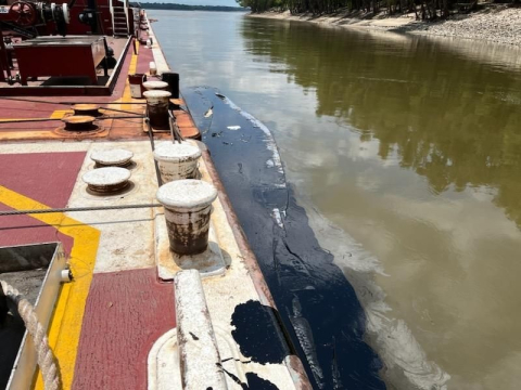 Barge with long oil spill streak in water beside it.