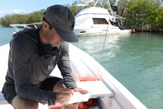 Man making written notes while sitting in a boat near a capsized boat.