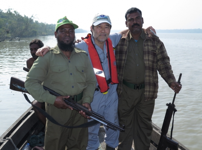 A man on a boat posing for a photo with two men holding guns.