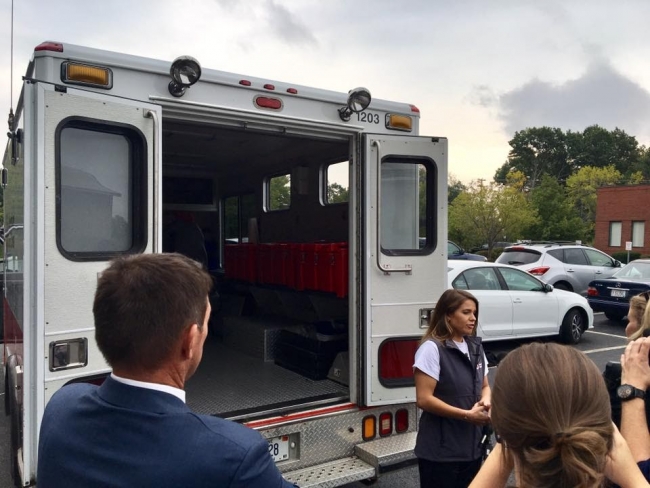 A person in front of an ambulance talking to a group of people. 