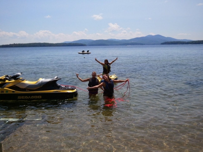 Three people in the water with a jet ski and an inner tube. 