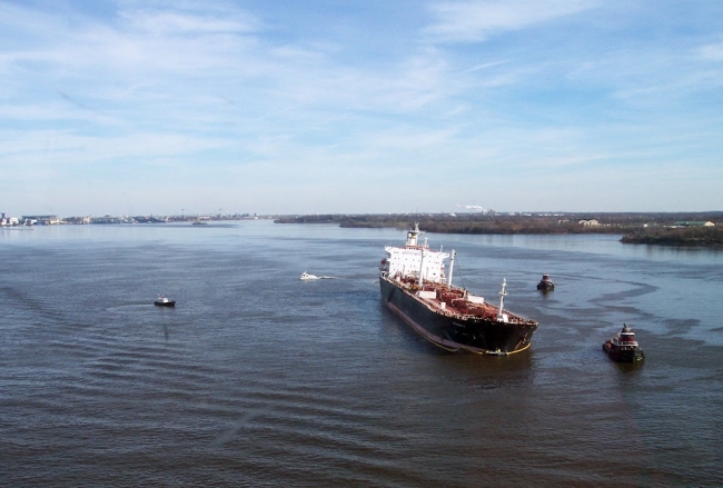 A large vessel with oil sheen visible in the water and several smaller vessels around it.