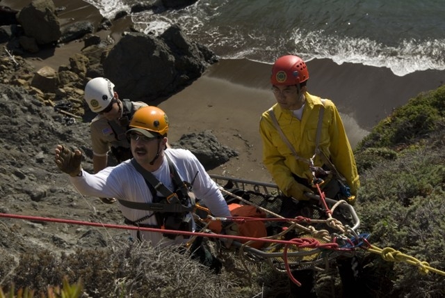A close-up shot of three people rappel down to a pocket beach.