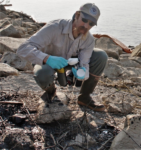A man collecting oil on a rocky beach. 