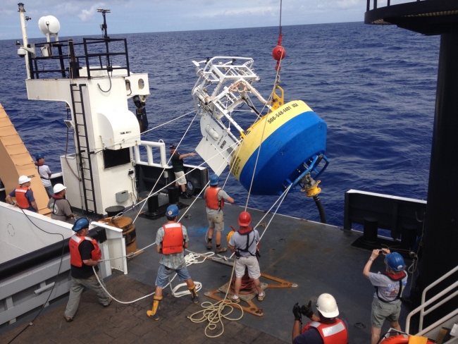 A crew of people aboard a ship hoisting up an piece of equipment from the water. 