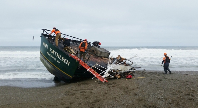 Several people standing on a wrecked, beached vessel. 