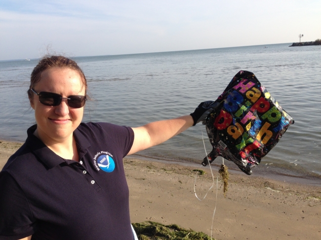 A woman on a beach holding up a birthday balloon. 
