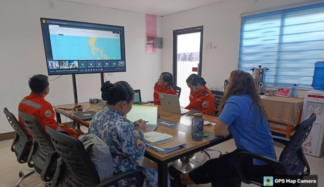 NOAA and Philippines response specialists convened around a conference table and viewing a map pulled up on a large screen.