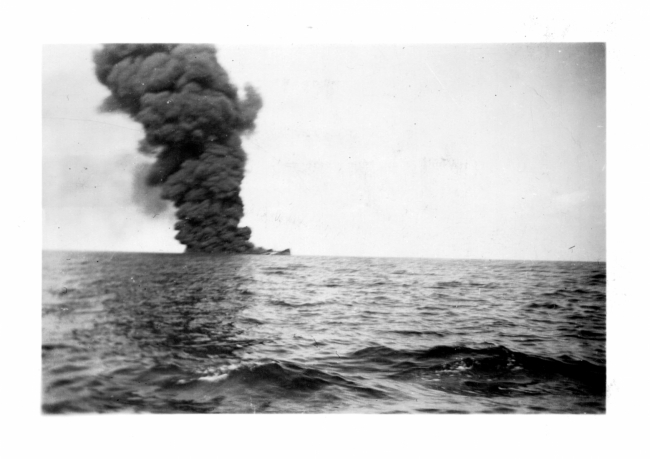 A black and white image of a plume of smoke coming from a vessel out at sea. 