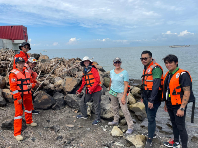 Response specialists from NOAA and the Philippines Coast Guard stand near an oil shoreline in the Philippines.