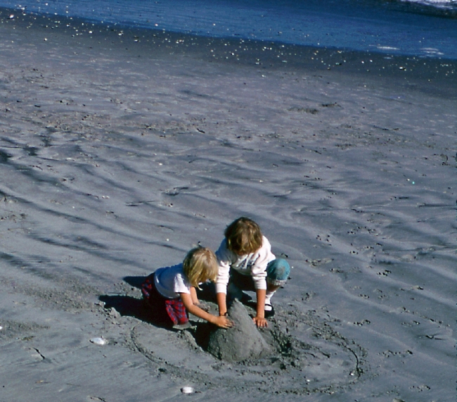Two kids making a sand castle on a beach.
