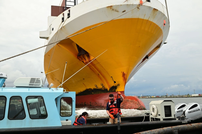 Workers in front of large disabled vessel.