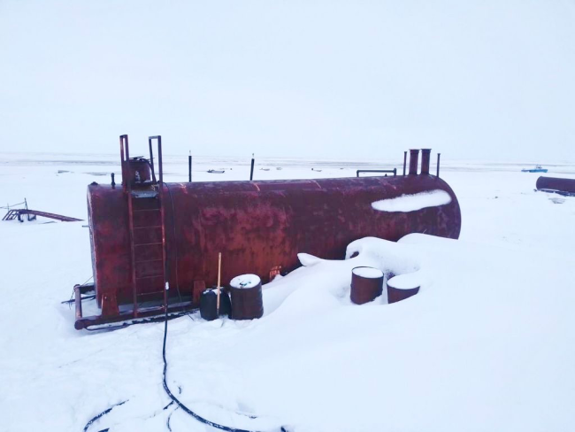 A large, red storage tank surrounded by a snowy environment in southwest Alaska.