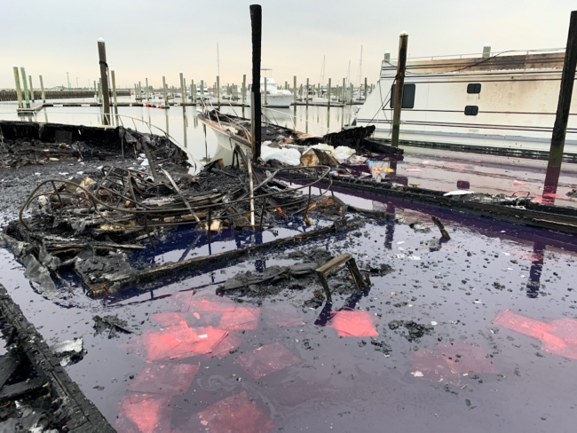 Two burned vessels partially submerged in a marina with a red liquid in the water. 