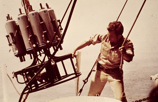 A man lifting a scientific instrument onto a vessel. 