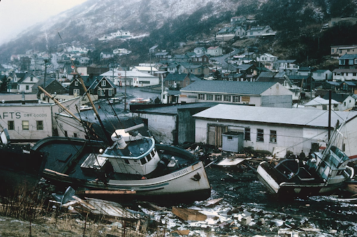 Commercial section of Kodiak, Alaska, in the aftermath of inundation by seismic sea waves. Boats from a harbor are displaced amongst the destruction of the section of the city..