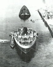 An old black and white photo of a vessel broken in half and partially submerged. 