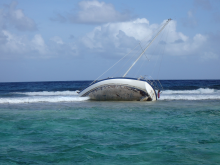 A grounded boat, turned on its side, with waves crashing into it. 