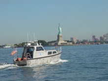 A boat in a body of water with the Statue of Liberty in the background.