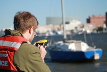 A person holding a device with a boat in the background. 