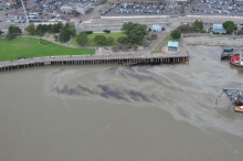 An aerial view of an oil sheen and oil in a body of water along an urban shoreline.