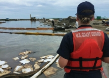 A person in a U.S. Coast Guard life preserver overseeing cleanup. 
