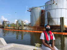 A person in a life vest with pollution boom around an industrial storage area.