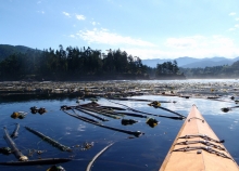 A view of a body of water with mountains in the background and the front of a kayak in the foreground. 