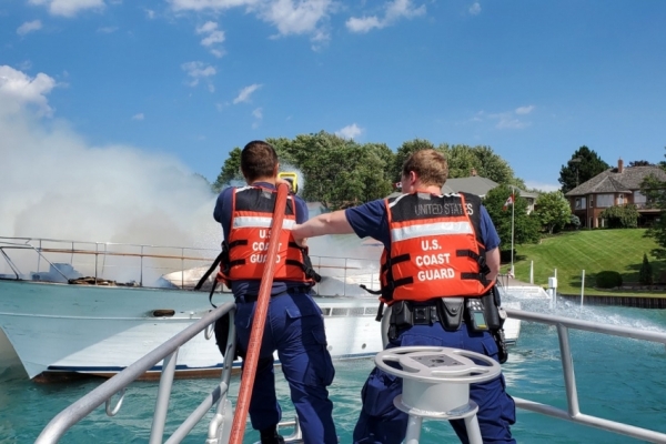 Two people in Coast Guard life jackets firing a water hose at a vessel. 