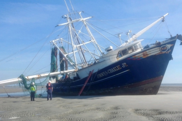 Two people on a beach looking at a grounded vessel. 