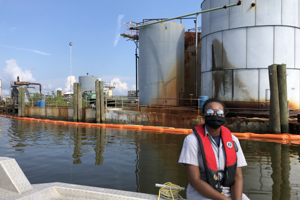 A person on a boat in front of an industrial area cordoned off with pollution boom.